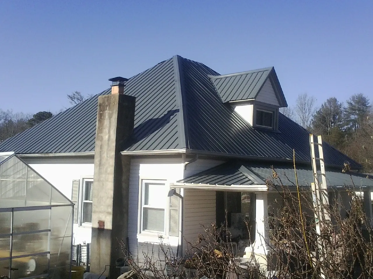 Dark blue standing seam metal roof on a white farmhouse with dormer — Slate & Tile Roof Repair by Roofing Brothers in Charles City