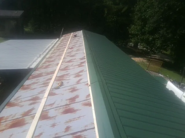 Old rusted panels beside newly installed green metal roofing — Wind Damage Roof Repair by Roofing Brothers in Charles City