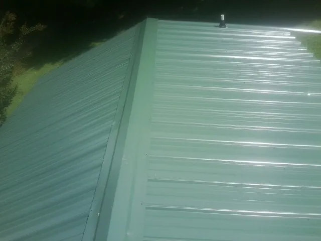 New green metal panels meeting at the ridge of a roof — Flat Roof Repair work by our crew in Charles City