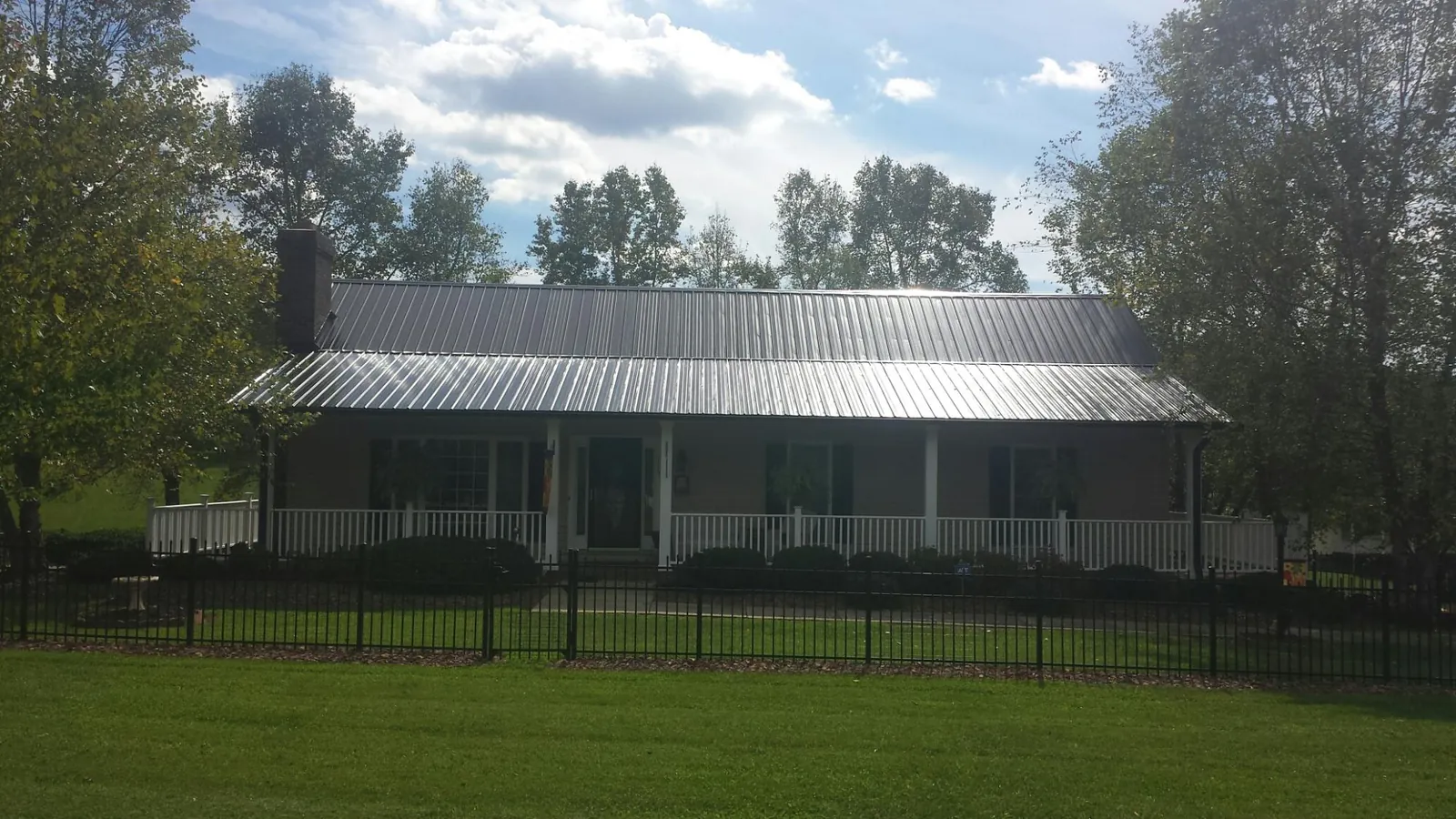 Gray metal roof on a brick ranch with a full width front porch — Gutter Guard Installation work by our crew in Charles City