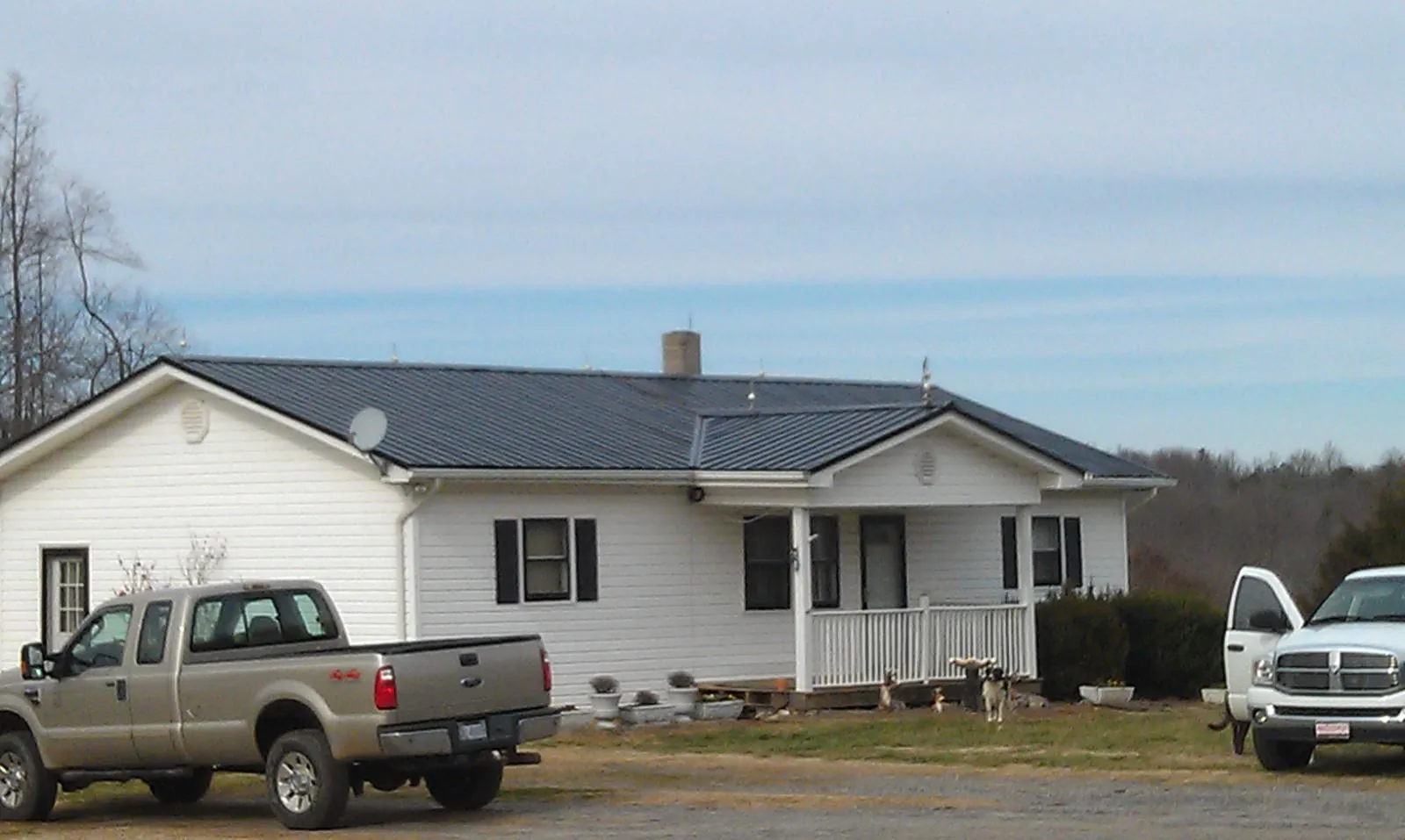 Finished dark metal roof on a white ranch home with work trucks parked in Charles City