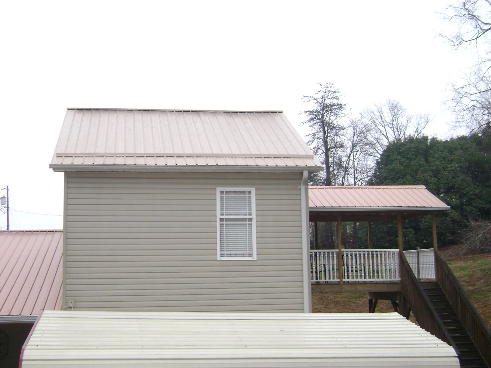 Tan metal roofs on a two story addition and attached porch, from a Roof Replacement job in Charles City