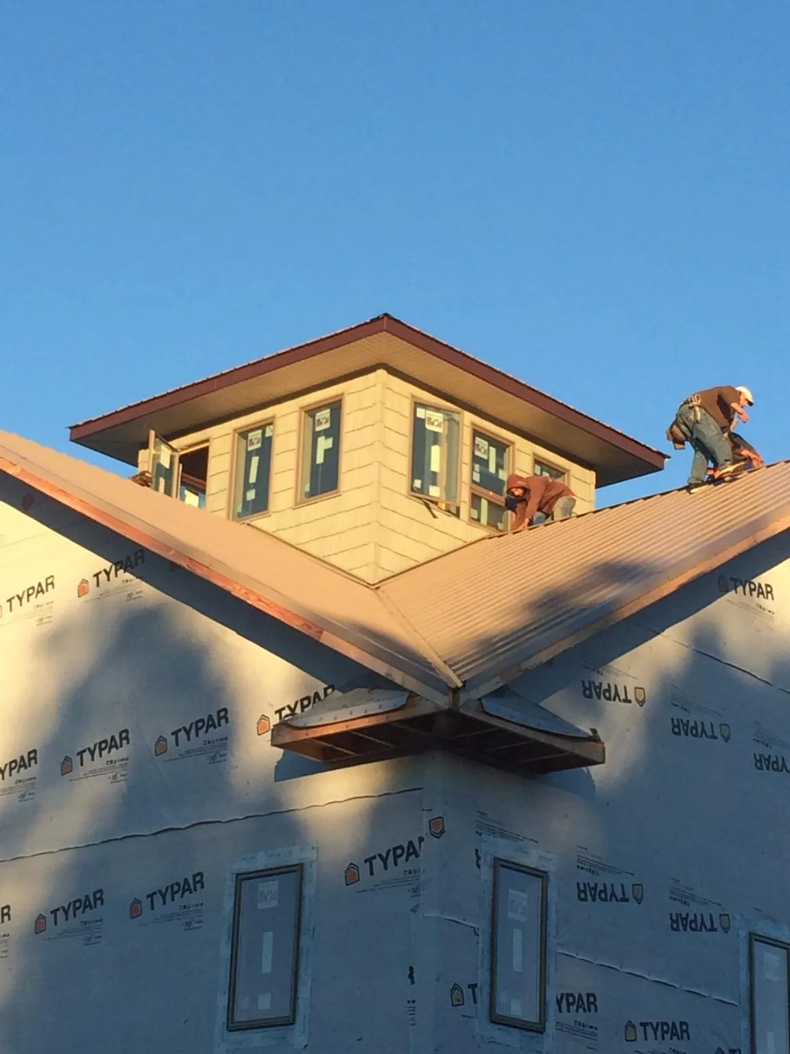 Roofers working around a rooftop cupola on a new metal roof at sunset — Roof Waterproofing in Charles City by Roofing Brothers